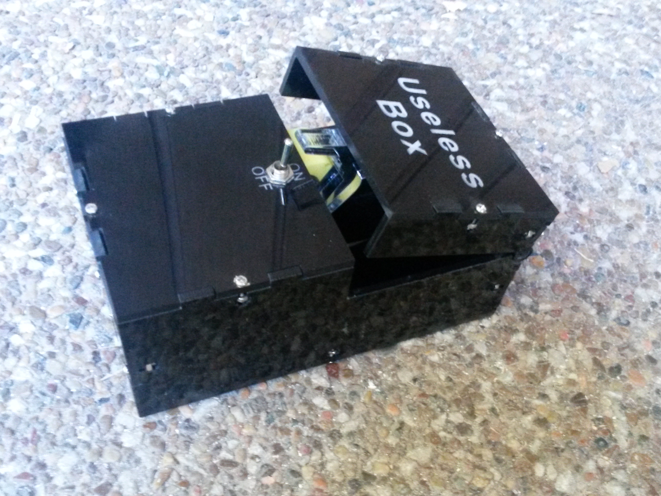 A black useless machine box with an on/off toggle switch and lid mechanism